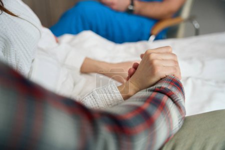 Téléchargez les photos : Vue recadrée de deux personnes sur un lit de maladie se tenant la main à l'intérieur - en image libre de droit