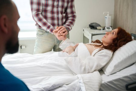 Photo for Caucasian woman patient looking at her husband while he holding her hand in hospital - Royalty Free Image