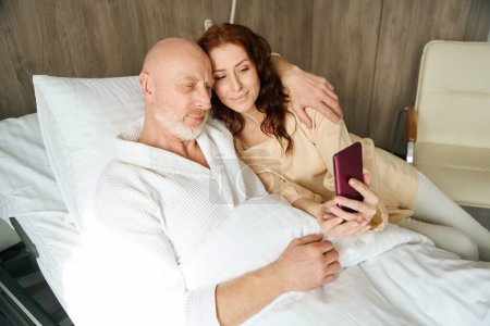Photo for Pretty woman browsing cellphone with her loved one in modern room of clinic - Royalty Free Image