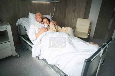 Foto de Hombre cansado y mujer pelirroja en ropa casual durmiendo en abrazo en el hospital - Imagen libre de derechos