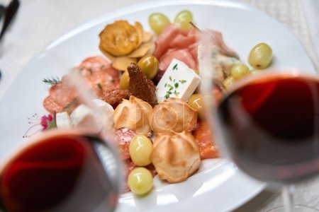 Foto de Primer plano de copas de vino caro y plato con muchos aperitivos diferentes servidos en mantel blanco en el restaurante - Imagen libre de derechos