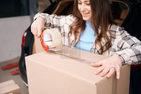Photo for Happy lady is packing cardboard boxes into the trunk of car in a storage warehouse - Royalty Free Image