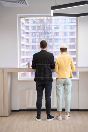 Photo for Back-view creative man and woman working on laptops at workplace near window, programming - Royalty Free Image