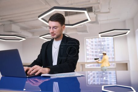 Photo for Concentrated young man working with graphs and data on laptop, using wi-fi in coworking space - Royalty Free Image