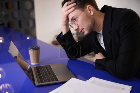 Foto de Analista masculino en gafas tiene problemas con la base de datos en el ordenador portátil, la pérdida de datos de los clientes, el espacio de coworking - Imagen libre de derechos