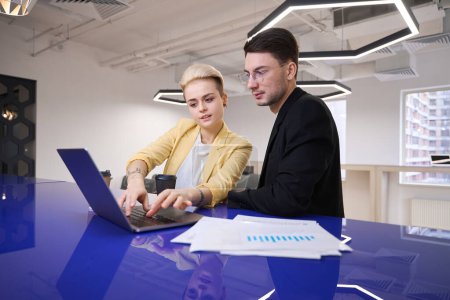 Téléchargez les photos : Homme et femme développant des logiciels sur ordinateur portable en utilisant les données du rapport, l'échange d'expérience de travail au club de l'espace ouvert - en image libre de droit