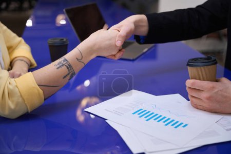 Foto de Hombre sacudiendo la mano femenina con tatuajes mirando por encima de los papeles con diagramas y datos, asociación, trato - Imagen libre de derechos