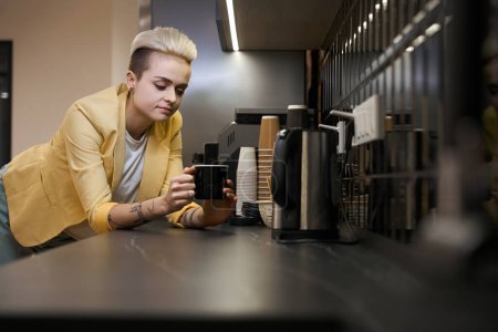 Photo for Stylish girl office worker enjoying taste and aroma of fresh beverage standing on kitchen of coworking space, comfort - Royalty Free Image