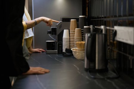 Foto de Mujer mostrando a nuevo oficinista cómo hacer café en la máquina de café en la cocina, bebidas gratis para los empleados durante el descanso - Imagen libre de derechos