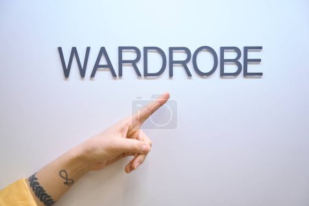 Photo for Close-up woman hand showing at wardrobe sign on door, cabinet in which clothes of workers hunging or storing - Royalty Free Image
