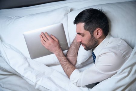 Photo for Man, without undressing, fell asleep in office clothes, next to a pillow is a working laptop - Royalty Free Image