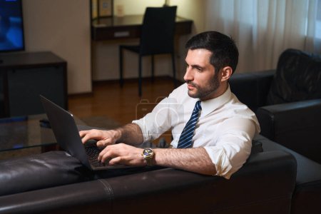 Téléchargez les photos : Homme d'affaires en voyage d'affaires travaille à partir d'une chambre d'hôtel, il utilise un ordinateur portable - en image libre de droit