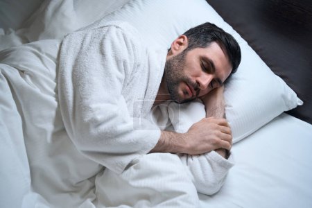 Téléchargez les photos : Fatigué mâle dort calmement au lit sur des oreillers doux, il se couche sur le côté - en image libre de droit