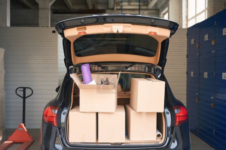 Photo for Cardboard big boxes with things are standing in the open trunk of a hatchback in a storage warehouse - Royalty Free Image