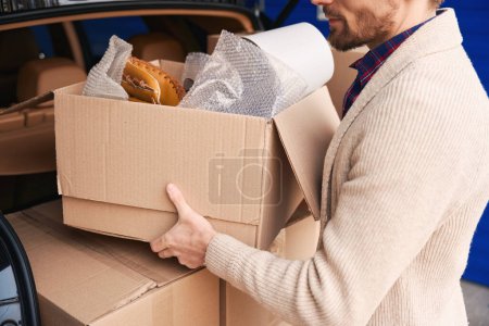 Foto de El hombre barbudo está poniendo cajas de cartón en el maletero de un coche en un almacén - Imagen libre de derechos
