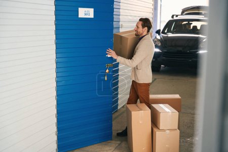 Photo for Young man is stacking cardboard boxes with things from a storage room in a warehouse - Royalty Free Image