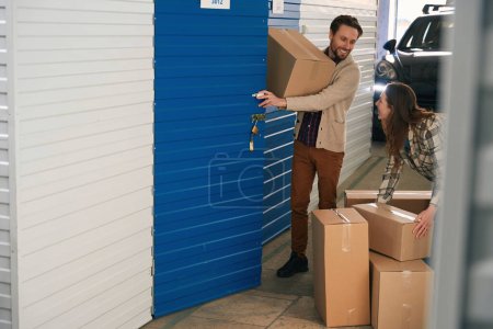 Foto de Pareja feliz están juntando cajas de cartón con cosas en el contenedor de auto almacenamiento - Imagen libre de derechos