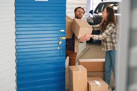 Photo for Happy couple are puting together cardboard boxes with things into self storage container - Royalty Free Image