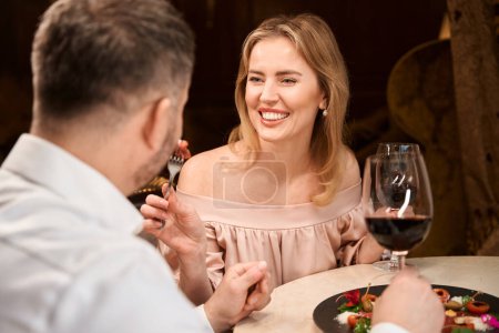 Photo for Beautiful woman feeding her husband while having romantic dinner in the luxury restaurant - Royalty Free Image