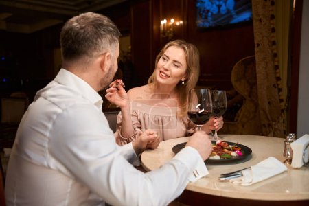 Foto de Hermosa dama sonriente su pasar tiempo con el marido mientras cena en la mesa en el restaurante de lujo - Imagen libre de derechos
