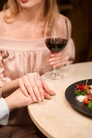 Téléchargez les photos : Gros plan d'un beau couple tenant chacun la main l'un de l'autre et dînant romantique à table au restaurant - en image libre de droit