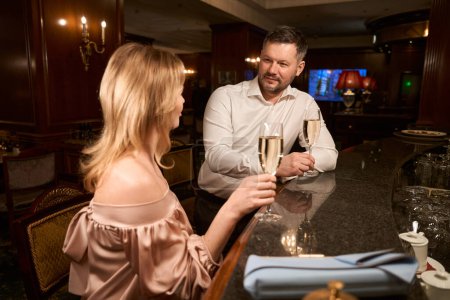 Téléchargez les photos : Heureux homme et femme avec des verres de vin mousseux communiquant entre eux lors d'un rendez-vous romantique au comptoir dans le bar - en image libre de droit