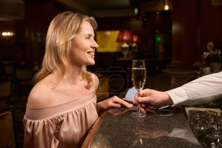 Téléchargez les photos : Homme barman servir verre avec du vin mousseux à charmante dame qui attend son homme au comptoir du bar - en image libre de droit