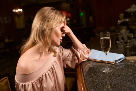 Téléchargez les photos : Dame élégante déçue assise seule avec un verre d'alcool et attendant son amie au comptoir du bar - en image libre de droit