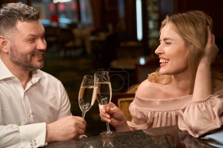 Téléchargez les photos : Homme souriant étranger et jolie femme se rencontrent et parlent avec du vin mousseux tout en étant assis au comptoir du bar - en image libre de droit