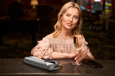 Foto de Señora feliz bebiendo vino espumoso mientras se divierte a solas y se enfría en el mostrador del bar - Imagen libre de derechos