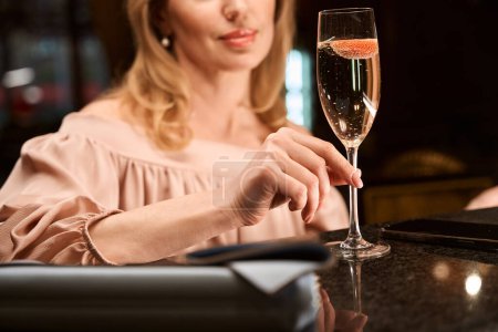 Téléchargez les photos : Photo recadrée de dame avec une coupe de champagne en attendant son amie au comptoir du bar - en image libre de droit
