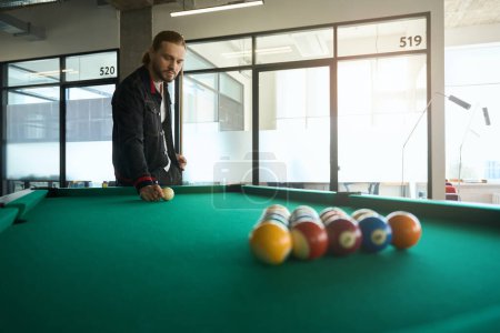 Photo for Male billiard player putting billiard ball on pool table and holding cue indoors - Royalty Free Image