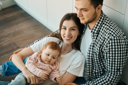 Photo for Joyful mom and dad are hugging the baby on floor in kitchen, remote work gives time to communicate with family - Royalty Free Image