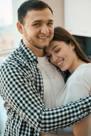Téléchargez les photos : Homme barbu joyeux embrassant tendrement sa femme, les gars en vêtements confortables occasionnels - en image libre de droit