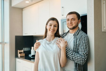 Photo for Happy young man tenderly hugs his wife by the shoulders, guys in comfortable home clothes - Royalty Free Image