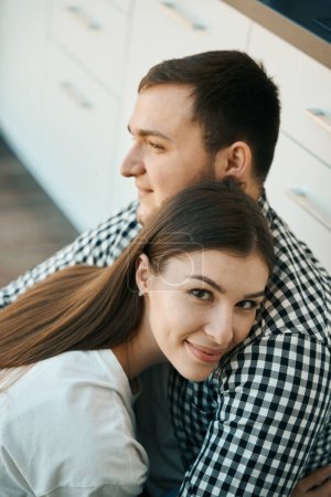 Photo for Beautiful man and woman are sitting, gently embracing, on the floor in the kitchen, guys in simple home clothes - Royalty Free Image