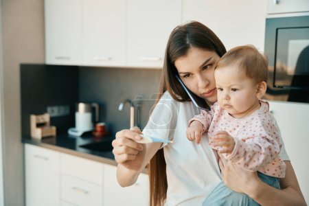 Photo for Worried mother holds a thermometer in her hands, she has a charming baby in her arms - Royalty Free Image
