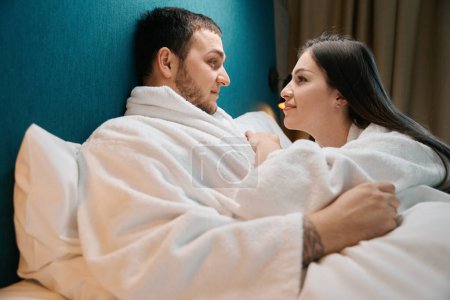 Téléchargez les photos : Couple en peignoirs se regardent avec amour, le couple luxueux sur le grand lit - en image libre de droit
