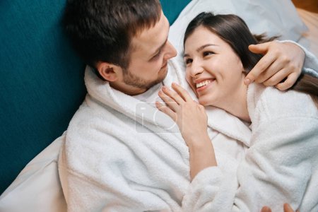 Téléchargez les photos : Femme tendre regarde avec amour son mari, le couple se prélasser sous les couvertures sur un grand lit - en image libre de droit