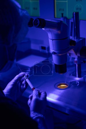 Téléchargez les photos : Ingénieur de laboratoire de reproductologie ajustant le support capillaire avant injection de sperme, injection intracytoplasmique de sperme icsi, lumière ultraviolette - en image libre de droit