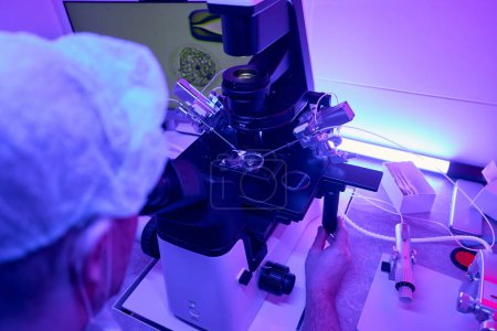 Photo for Genetic laboratory worker looking on cell at display connected with microscope and using micromanipulator to do genetic biopsy - Royalty Free Image