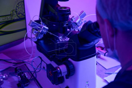 Embriólogo hombre que trabaja con micromanipulador mirando al microscopio, haciendo biopsia de embriones para excluir mutaciones y anormalidades