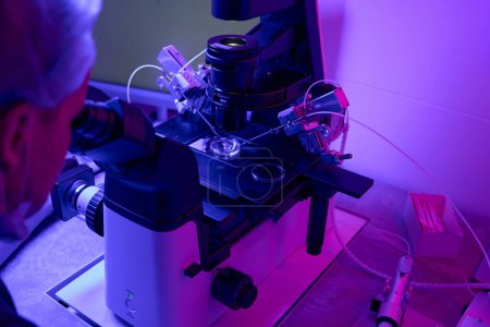 Téléchargez les photos : Travailleur biolaboratoire regardant le microscope faire une biopsie cellulaire avec micromanipulateur, effectuant un diagnostic génétique préimplantatoire - en image libre de droit