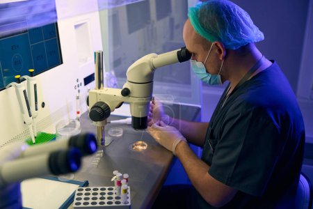 Foto de Embriólogo investigando células femeninas y preparándolas para biopsia y fertilización, trabajando en biolaboratorio con microscopio y monitores digitales - Imagen libre de derechos