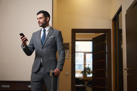 Foto de Hombre en un traje de negocios se comunica en un teléfono móvil, un hombre tiene una maleta de viaje - Imagen libre de derechos