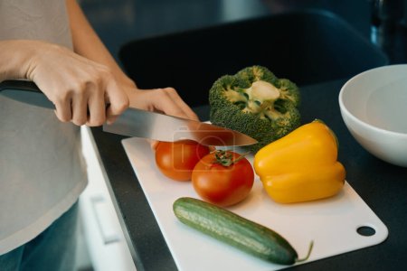 Foto de Mujer corta verduras maduras para una ensalada saludable, utiliza una tabla de cortar y un cuchillo afilado - Imagen libre de derechos