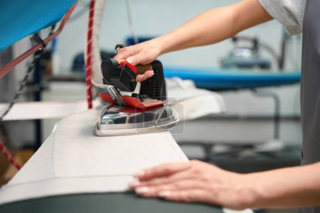 Photo for Woman laundry service worker carefully ironing clothes with special iron with steam to get rid of wrinkles, close-up - Royalty Free Image