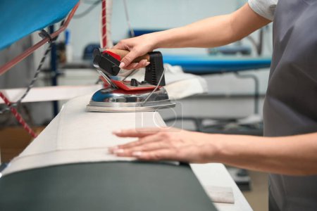 Photo for Close-up woman laundry office operator carefully ironing garment with hot industrial iron, relaxing wrinkles - Royalty Free Image