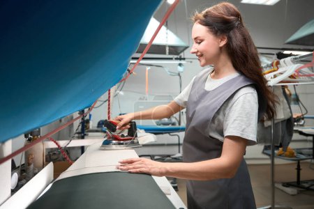 Photo for Skilled woman dry cleaner service worker ironing cloth after pressing on steam board, post treatment - Royalty Free Image