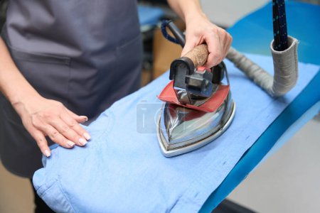 Photo for Close-up woman using hot iron to remove wrinkles from shirt, professional electric appliance at dry-cleaning office - Royalty Free Image